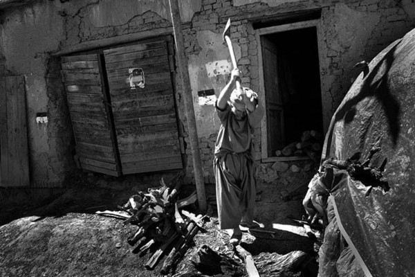A man in Bagram cuts up the wood collected during the day. On the wall behind him is a painted code from the deminers; red and white. Red is the colour that marks out the dangerous side, and the white colour marks out the safe side. In this picture it means that this side of the wall is cleared, but not the inside of the compound : Demining in Kabul : Charlotte Oestervang Photography